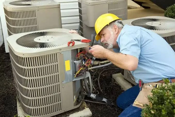 Technician examining wiring inside an outdoor HVAC unit